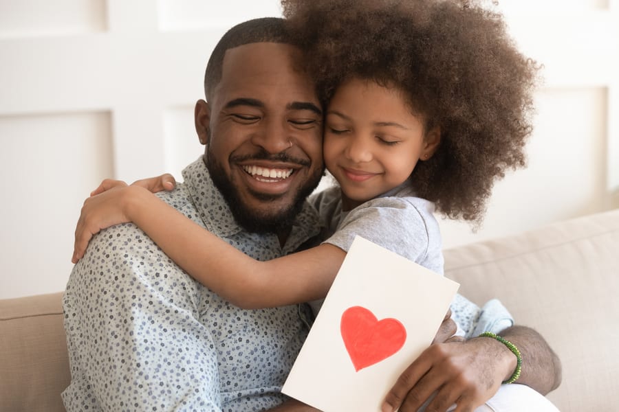 A father and daughter hugging, holding a card with a hand-drawn heart on it